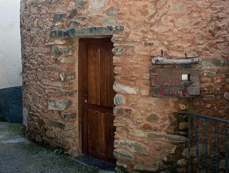Fachada de mampostería de piedra y pizarra de la Casa Chica, en la alquería de Erías, con puerta de madera y cartel pintado a mano.